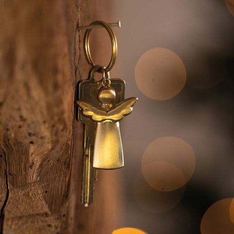 Gold key with angel charm attached to a wooden surface
