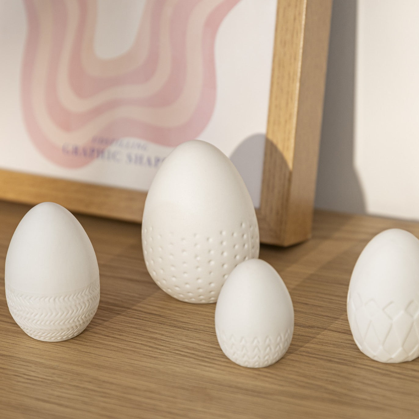 Four White Porcelain Embossed Easter eggs on a wood table with a picture behind.