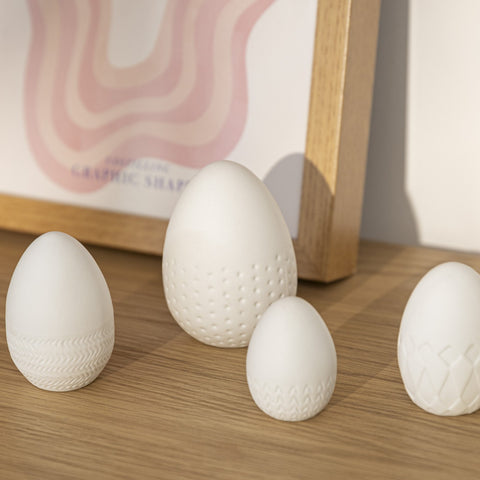 Four White Porcelain Embossed Easter eggs on a wood table with a picture behind.