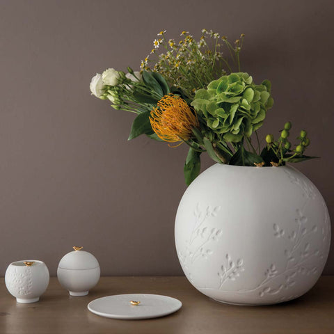 White porcelain vase with floral arrangement on a brown surface against a dark brown background with flock of birds collection to the side