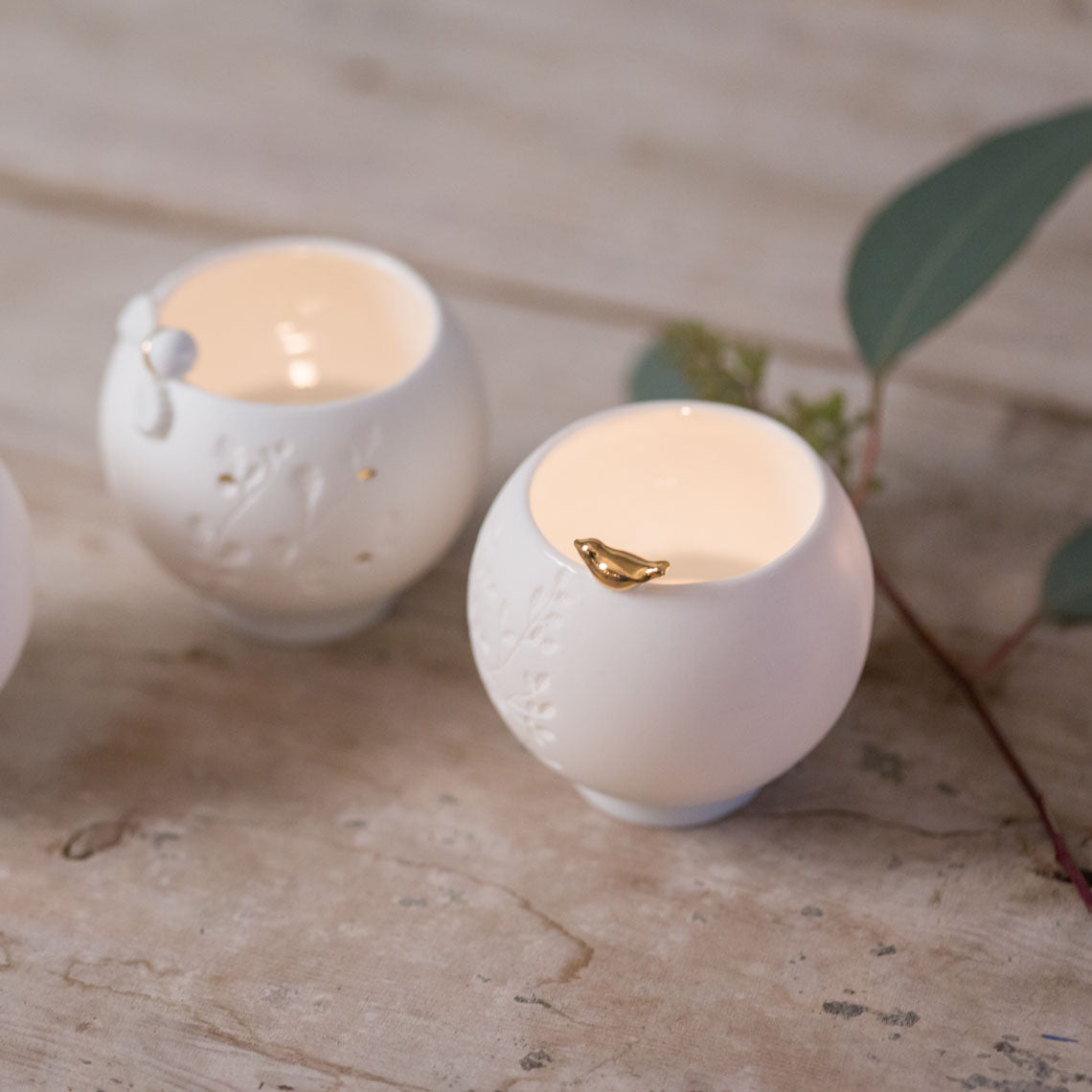 Two white porcelain candle holders with lit candles on a textured surface.