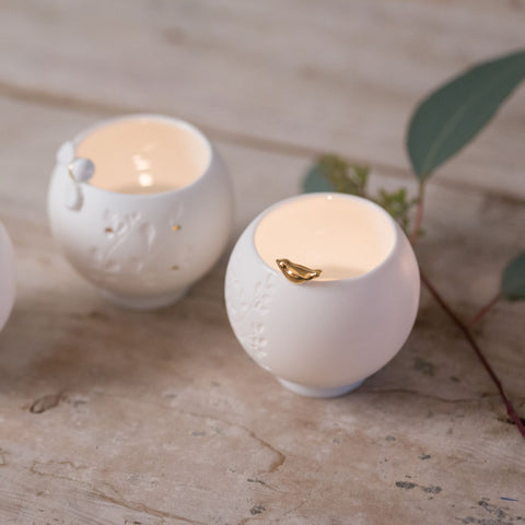 Two white porcelain candle holders with lit candles on a textured surface.