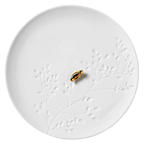 White porcelain plate with embossed design and a small black and gold object on a white background