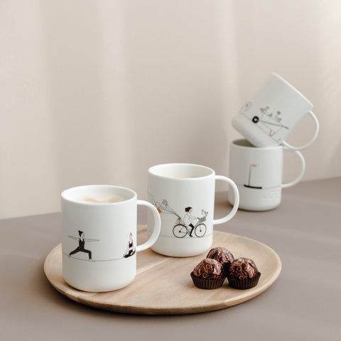 White mugs with black illustrations on a wooden tray with pastries against a beige background