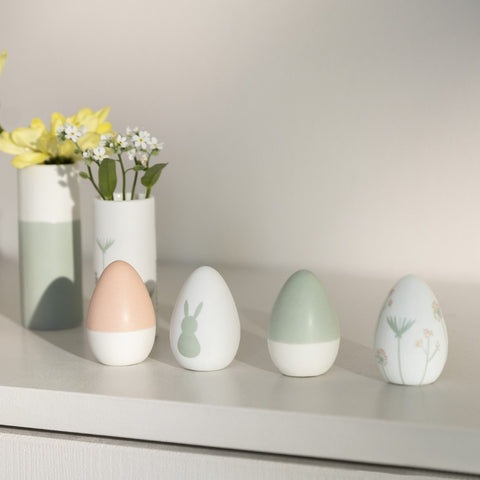 Four Porcelain Easter Eggs on a shelf with vases in the background.
