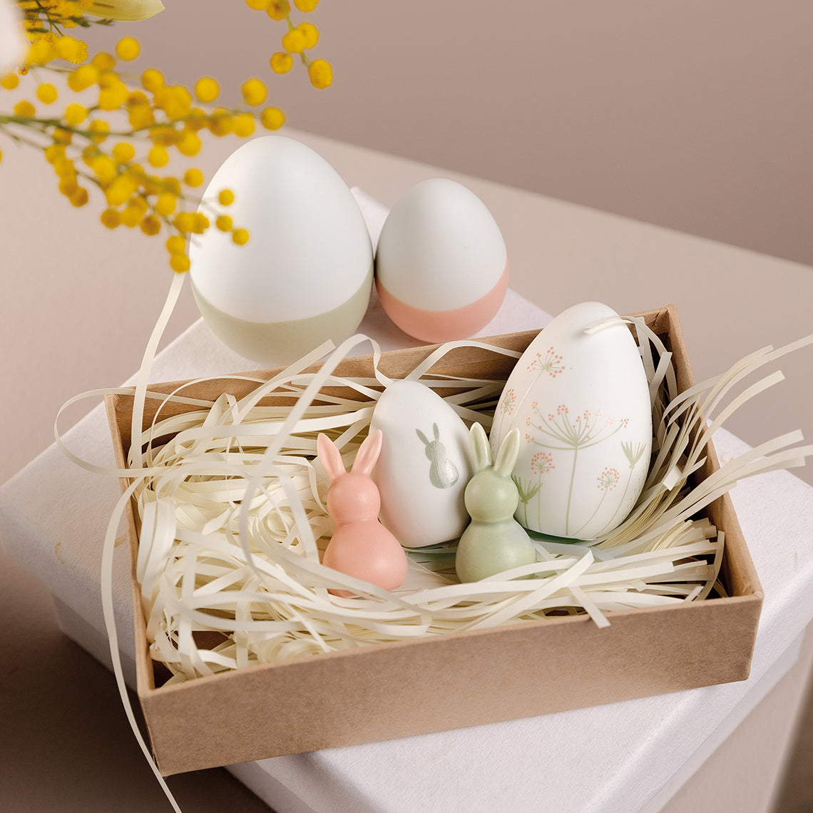 Decorative Porcelain Easter Eggs and bunnies in a box with straw on a light background