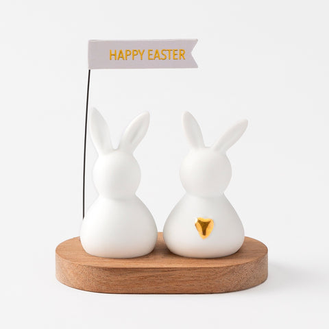 R17463 Two porcelain bunnies on an acacia wood tray holding a happy easter sign.