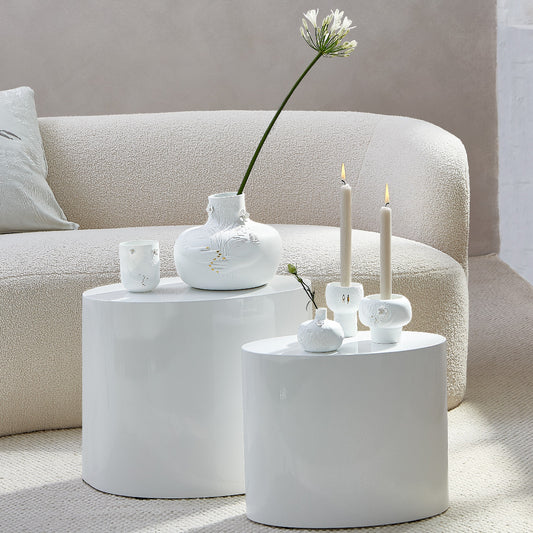 Picture Stories White porcelain vases and candle holders on a round white table in a living room settin.