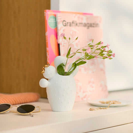 White Porcelain Cactus Vase with a small plant on a surface with sunglasses and a magazine in the background.