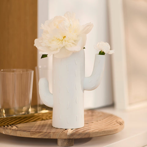White cactus-shaped vase with a single white flower on a wooden surface.