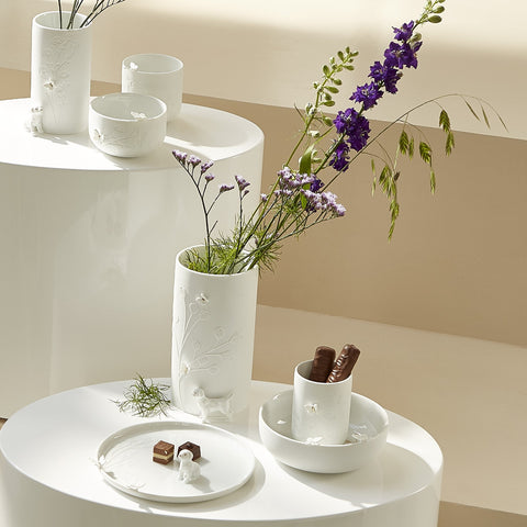 White porcelain items including tealight holders, bowls, plates and a vase with flowers on a white surface.