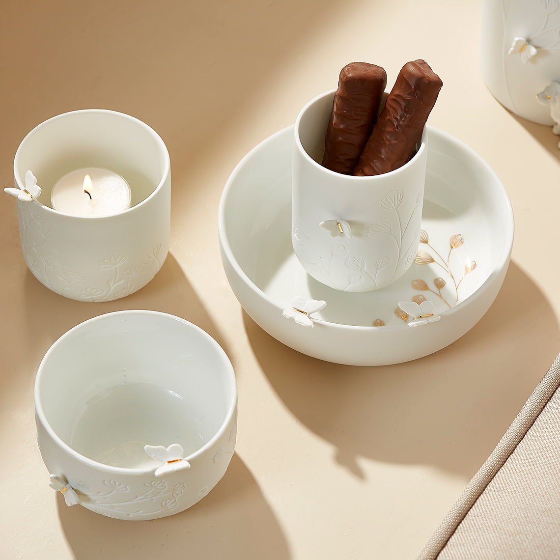 Set of white porcelain decorative items with decorative elements, including butterflies, on a beige surface.
