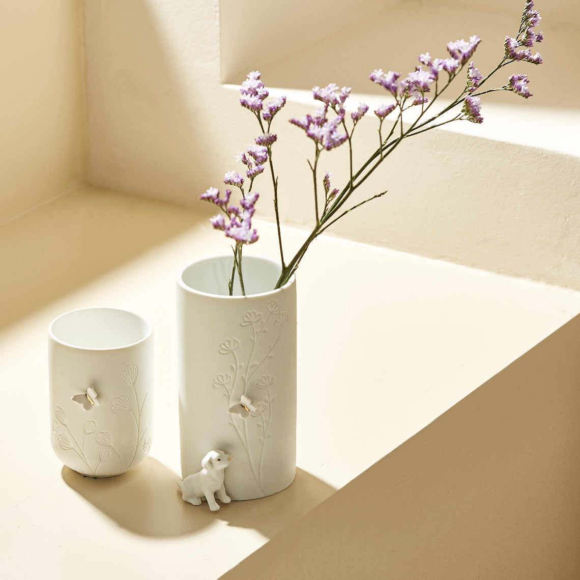 White porcelain vase and tealight holder with floral designs and butterflies and puppies on a beige surface