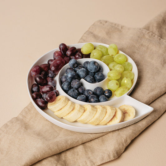 Snacktime platter with grapes, blueberries, and bananas on a beige background
