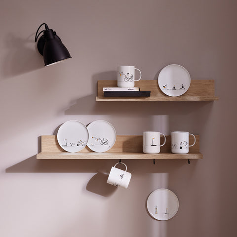 Wooden shelves with porcelain Hobby plates and mugs against a beige wall.