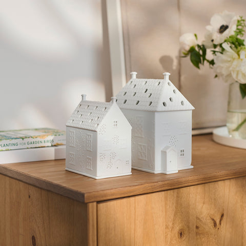 Two white house-shaped lanterns on a wooden surface with a blurred background