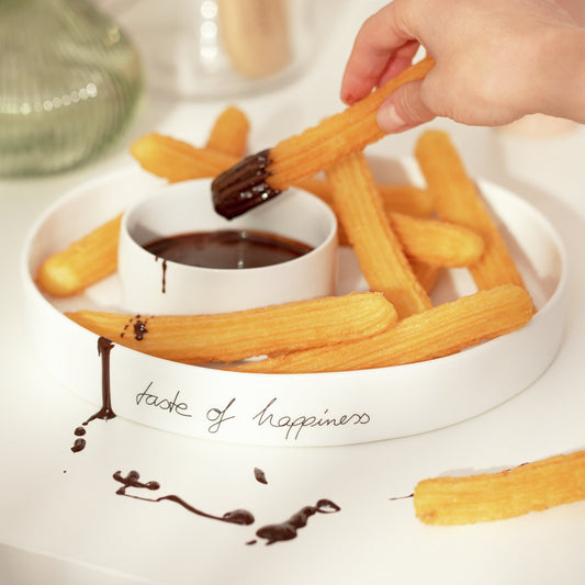 Churros being dipped into chocolate sauce with a hand holding one churro.