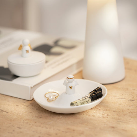 Small white dish with a ring and small bottle on a wooden surface