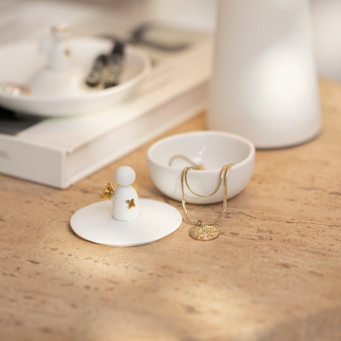 White jewelry canister with a small white angel and gold necklace on a wooden surface.