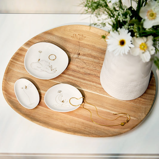 Garden of Heaven mini dishes with delicate gold floral engravings are arranged on a round wooden serving tray, styled with gold necklaces and rings next to a white ceramic vase of daisies.