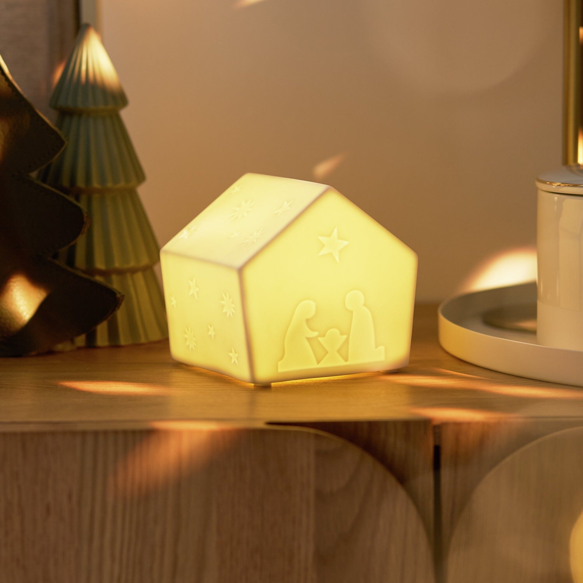 Porcelain LED Lamp Nativity House on wood shelf with light on. 
