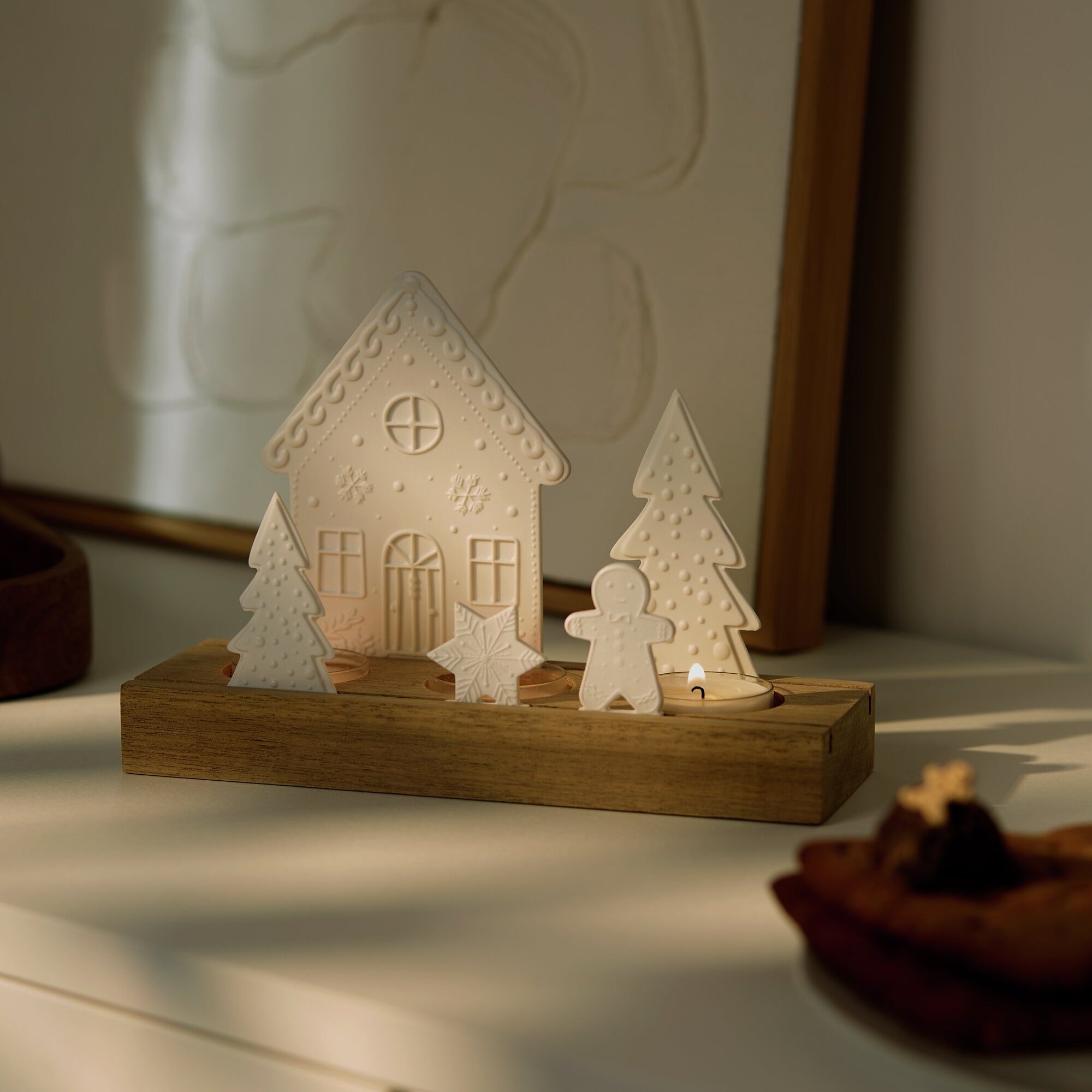 Porcelain and Acacia Wood Gingerbread themed tealight holder in a dim room with the tealight candles lit. 