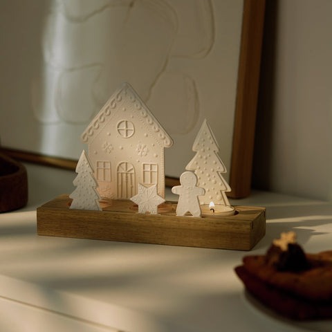Porcelain and Acacia Wood Gingerbread themed tealight holder in a dim room with the tealight candles lit. 