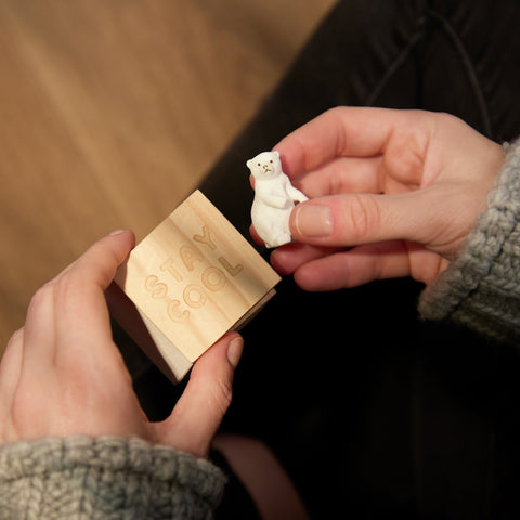 Person holding a small white polar bear figurine and a wooden box with engraved text.