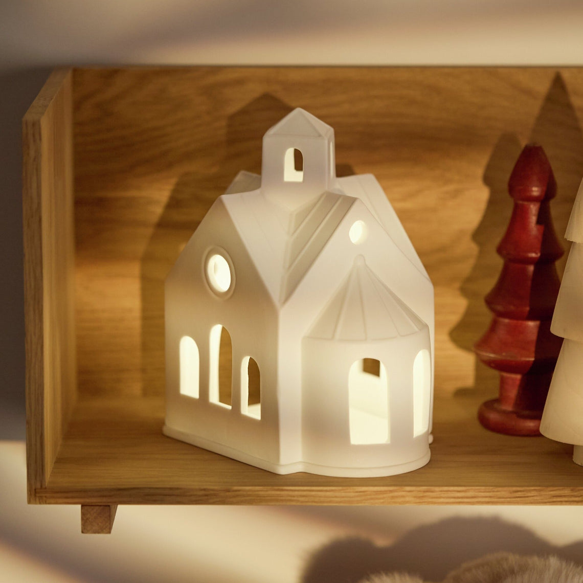 White house-shaped lantern on a wooden shelf with a warm glow