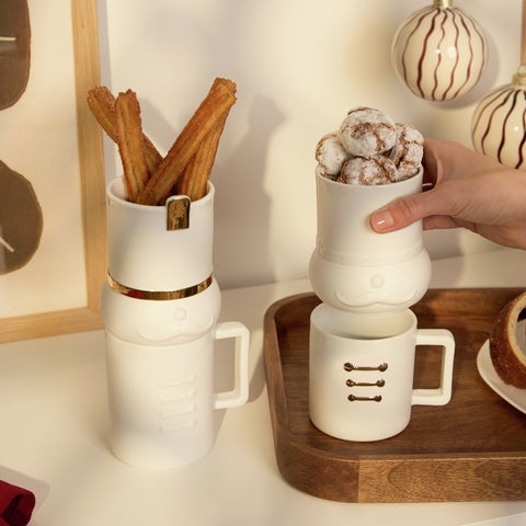 Nutcracker Mug and Treat Sets on a kitchen counter with treats in the containers and christmas balls hanging behind.