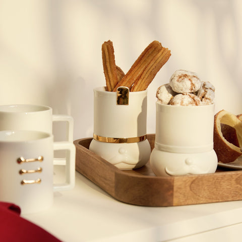 Nutcracker mug and treat set with treat containers placed on a wood tray and mugs sitting beside them on a kitchen countertop.
