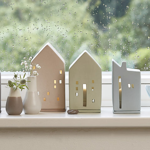 Decorative house-shaped lanterns on a windowsill with a rainy window background